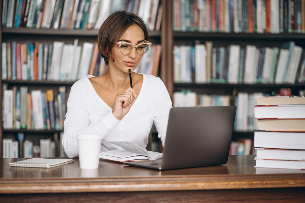 Woman studying on laptop in library with books and coffee cup on desk