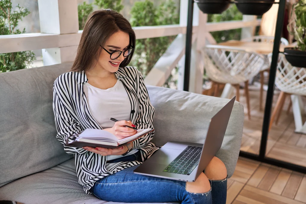 smiling woman taking notes with laptop on couch