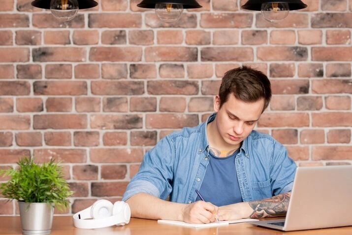 Man studying and taking notes with laptop at desk